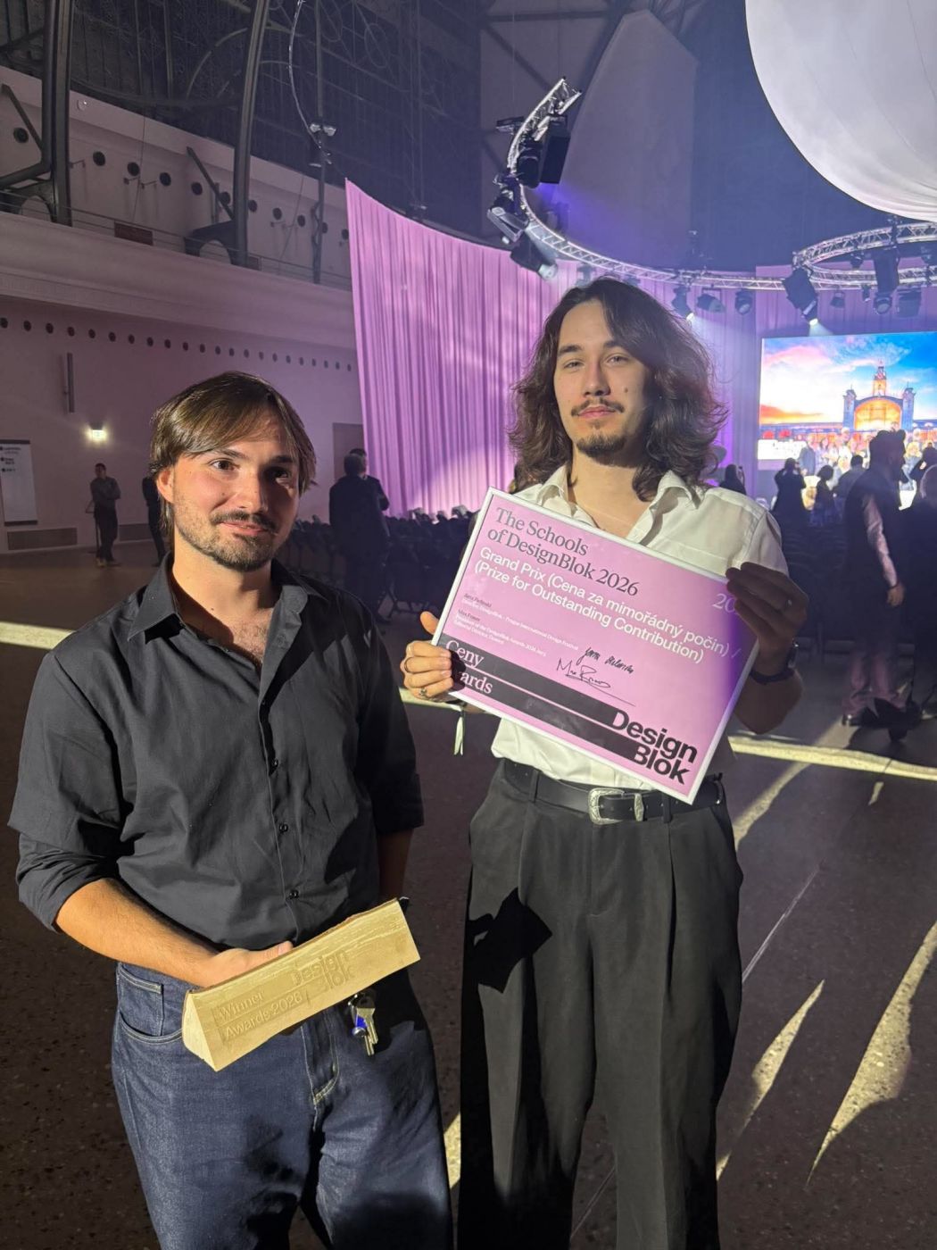 Dvaja účastníci slávnostného odovzdávania cien Designblok 2026 s trofejou a ružovým diplomom The Schools of Designblok 2026 – Grand Prix, Cena za mimoriadny počin.