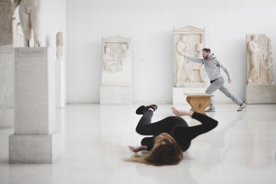 Dvaja performeri v galérii so sochami – jedna osoba leží na podlahe, druhá sa pohybuje v dynamickej póze.