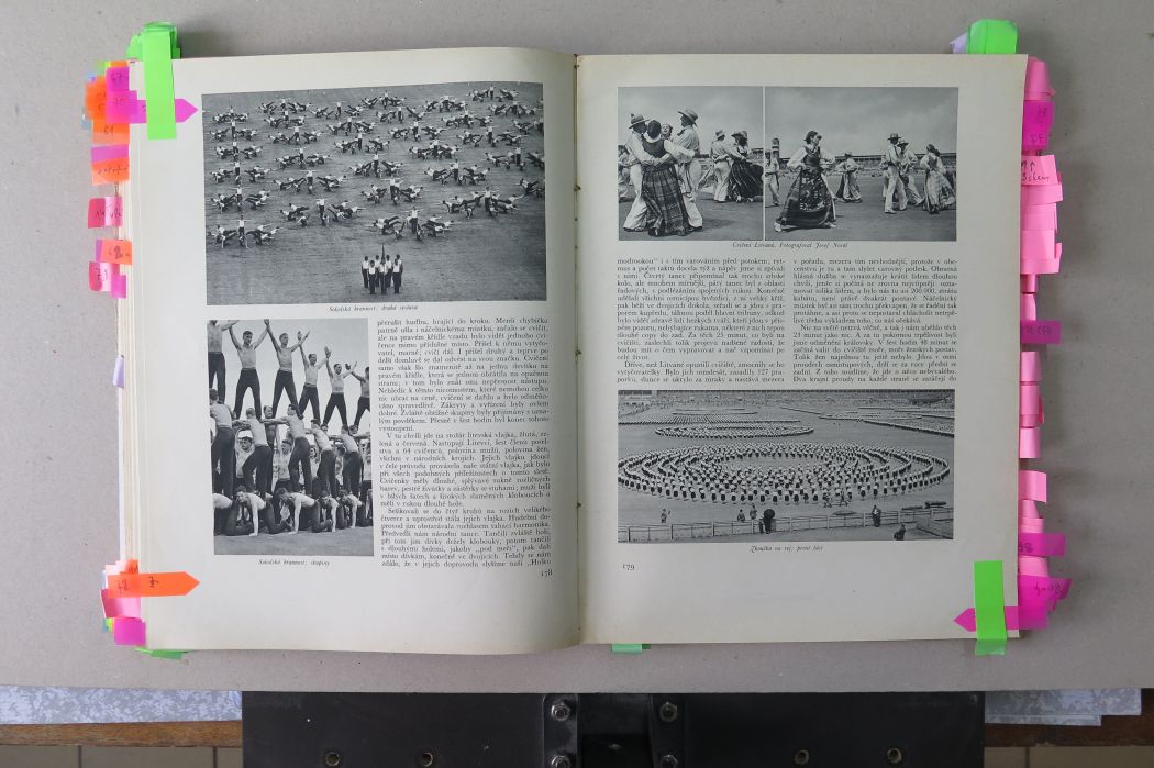 Otvorená kniha s historickými čiernobielymi fotografiami a poznámkami označenými farebnými lístkami.